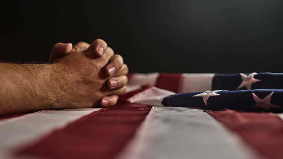 praying hands resting on top of an American flag