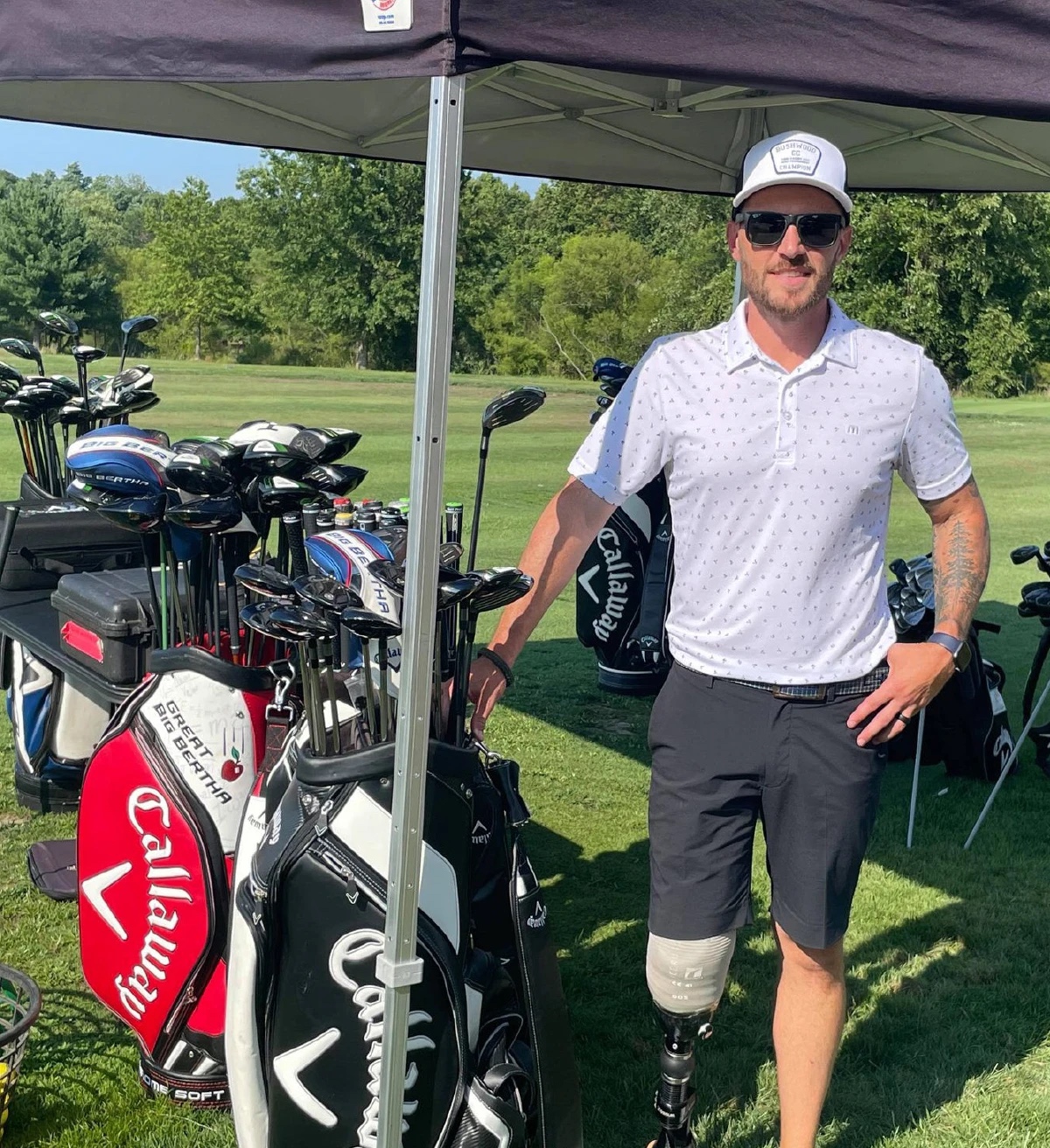 veteran amputee standing next to golf clubs under a tent on a golf course